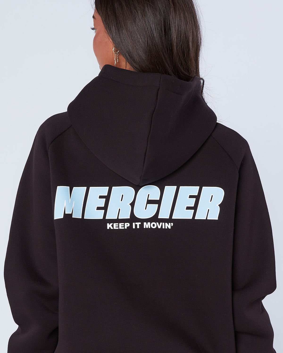 Person wearing a black hoodie with 'Mercier Keep It Movin'' text on the back against a white background